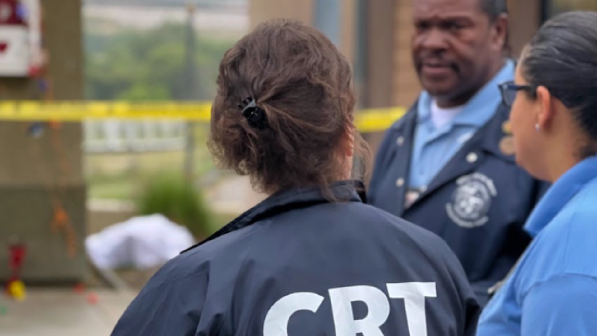 The letters CRT can be seen on the back of a volunteer standing outside an indistinct crime scene 