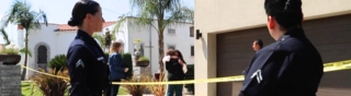 Two LAPD officers stand by as two family members embrace behind yellow crime tape.